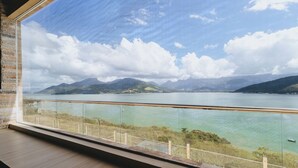 Quarto com uma grande janela com vista para um lago e montanhas.