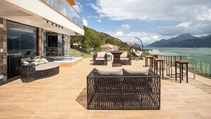 Um pátio moderno ao ar livre com móveis de vime, uma cadeira suspensa e vista para um lago e montanhas.