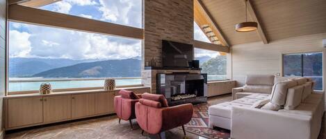 Un salón espacioso con chimenea, ventanas amplias que ofrecen vistas a la montaña y una zona de estar acogedora.