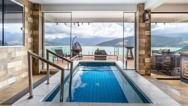 Piscina interior moderna com vista clara para um lago e montanhas.