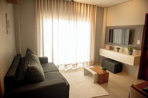 Een moderne woonkamer met een donkere bank, een houten salontafel en een flatscreen televisie aan de muur.