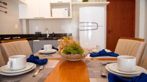 A dining table set for four with white plates, blue napkins, and a glass bowl with green foliage. - Beachfront apt: balcony, pool, pet friendly (Japaratinga)
