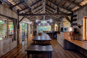 A rustic kitchen with a wooden table, a brick wall, and a sign reading "NCHO ACONCHO".