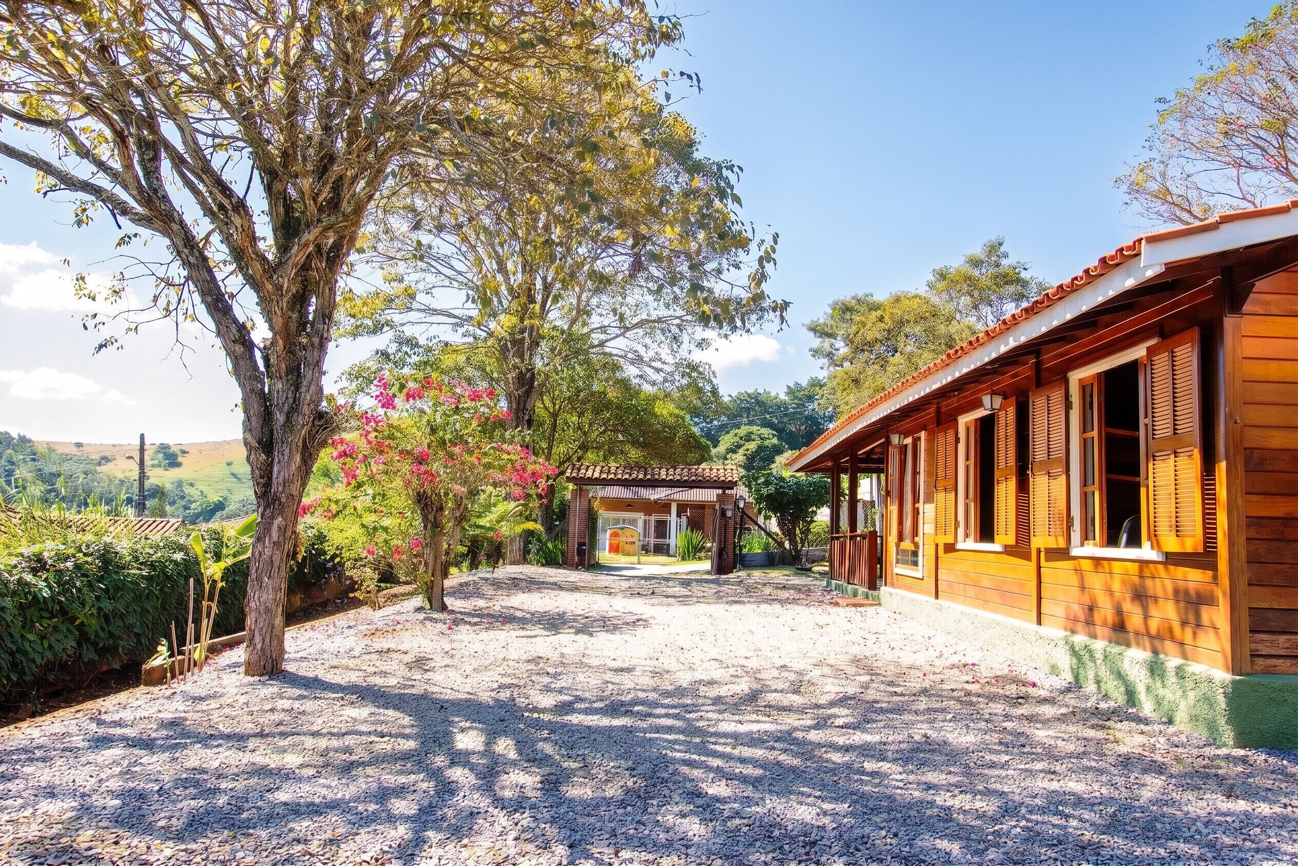 Uma casa de madeira com um caminho de cascalho, rodeada por árvores e um céu claro.