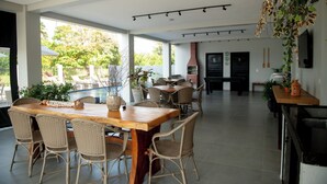 A spacious indoor area with a wooden dining table surrounded by wicker chairs, a kitchen area with a grill, and large windows offering a view of the outdoors. - Apto com Piscina e Churrasqueira Perto da Praia (Japaratinga)
