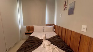 A hotel room with a bed, a bedside table with a plant, and a wall-mounted outlet. - Apto com Piscina e Churrasqueira Perto da Praia (Japaratinga)