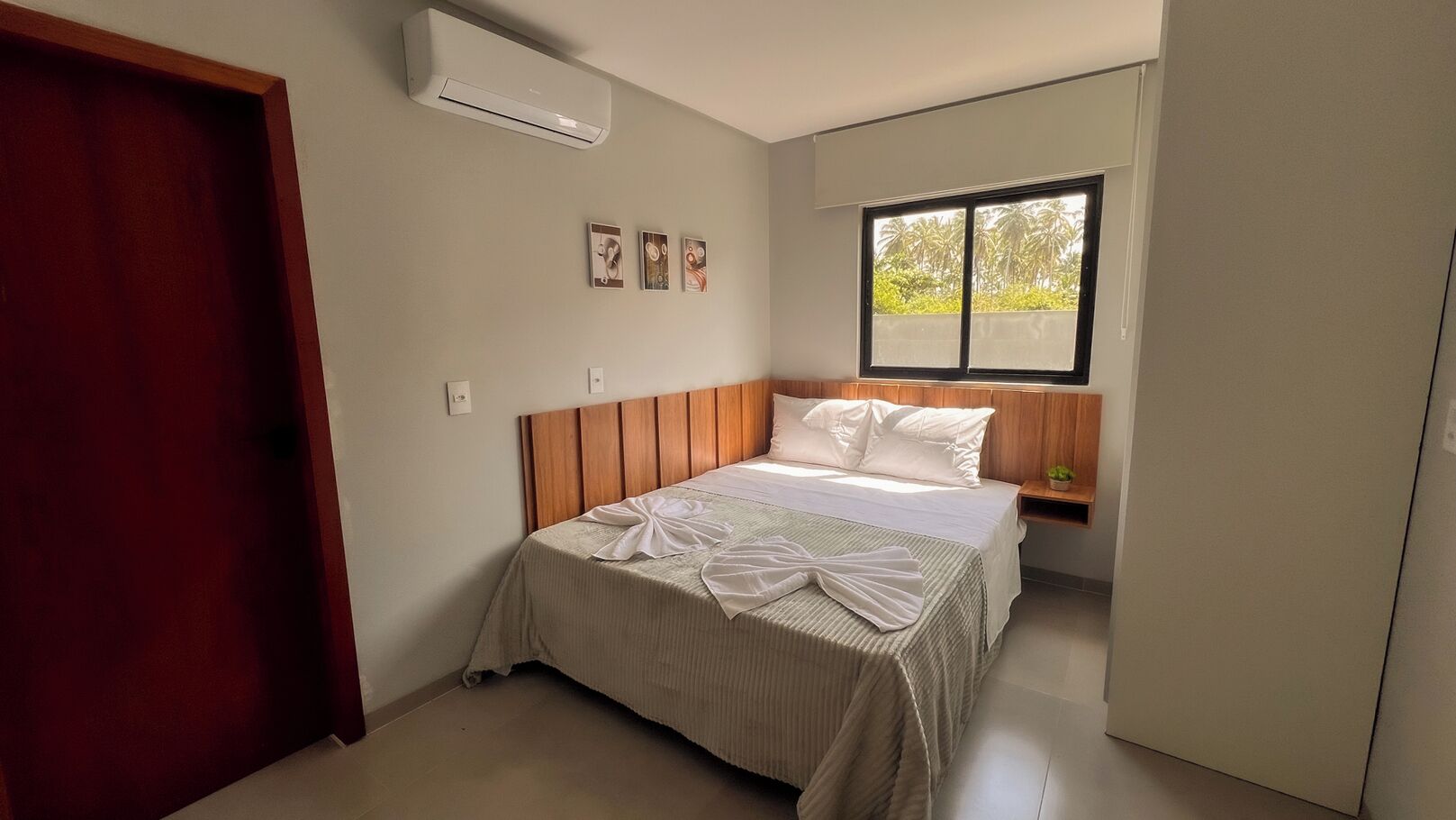 A bedroom with a bed, a window, a nightstand, and an air conditioning unit.