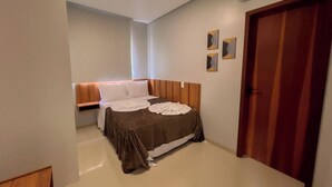 A bedroom with a bed, a wooden headboard, a wardrobe, and an air conditioning unit. - Apto Vista Mar a 100m da Praia de Japaratinga (Japaratinga)