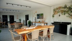 Een ruime eethoek met een houten tafel en rieten stoelen, een keuken met een zwart aanrechtblad, en een hangende plantdecoratie.