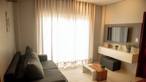 Een moderne woonkamer met een donkere bank, een houten salontafel en een flatscreen televisie aan de muur.