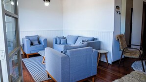 A living room with a blue sofa set, a small round table, and a furry chair. - Casa com lareira, Wi-Fi e varanda com vista (Campos do Jordão)