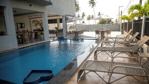 A swimming pool with lounge chairs and umbrellas, surrounded by a patio area with tables and chairs. - Apt Vista Mar 100m da Praia Piscina 2 Suítes (Japaratinga)