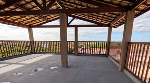 Ein offenes Pavillon mit Betonboden und Metallgeländern, das auf eine Landschaft mit Gebäuden und Grünflächen blickt.