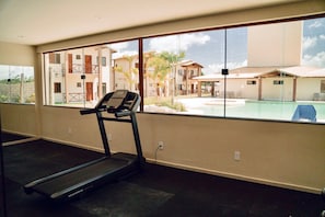 Ein Fitnessraum mit Laufband, großen Fenstern und Blick auf einen Pool und Gebäude.
