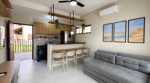 A modern kitchen with a central island, a dining area with chairs, a grey sofa, and three framed landscape paintings on the wall. - Dunas de Amaro Chalet: 3 Suites, Pool & Viewpoint (Santo Amaro)