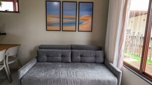 A grey sofa with a cushioned backrest, a white chair, and a window with curtains.
