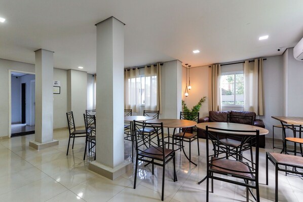 A spacious dining area with multiple tables and chairs, large windows with curtains, and a modern ceiling design.
