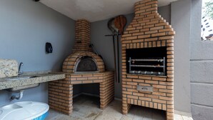 Tiilistä rakennettu ulkokeittiö, jossa on pizzauuni, grilli, pesuallas ja roskakori.