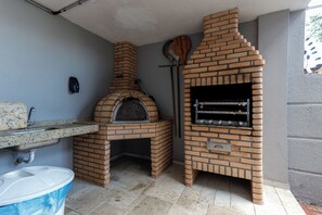 A brick-built outdoor kitchen with a pizza oven and a grill, a sink, and a trash bin.