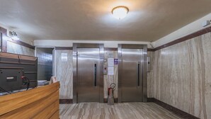 A modern elevator area with marble walls, a wooden reception desk, and stainless steel elevators. - Studio com Wi-Fi e Ar a 45m da Praia de Copacabana (Rio de Janeiro)