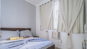 A bedroom with a bed, curtains, a bedside table, and a wall-mounted heater. - Studio com Wi-Fi e Ar a 45m da Praia de Copacabana (Rio de Janeiro)