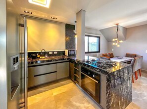 A modern kitchen with a marble countertop, stainless steel appliances, and a dining area with a table and chairs. - Casa de Inverno em Campos com Lareira e Jacuzzi (Campos do Jordão)