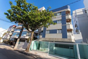 A multi-story residential building with balconies, a tree in front, and a glass entrance. - Apto Pet Friendly com Garagem na Enseada Azul (Guarapari)