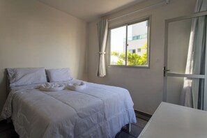 A hotel room with a bed, a window with curtains, and a door. - Apto Pet Friendly com Garagem na Enseada Azul (Guarapari)