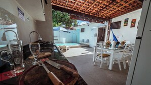 Una cocina con tabla de cortar de madera, un cuchillo y una copa de vino. Se ve una piscina al fondo.