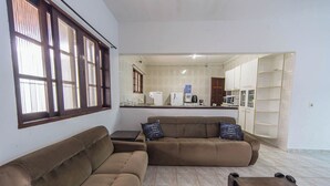 A living room with a sofa, a coffee table, and a TV stand. There is a kitchen area in the background with a microwave and a coffee machine. - Casa com Piscina e Garagem a 550m da Praia (Peruíbe)