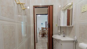 A bathroom with a sink, mirror, and shower. There is a wooden door leading to a dining area. - Casa com Piscina e Garagem a 550m da Praia (Peruíbe)