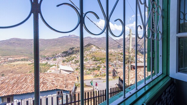 Een balkon met sierijzeren hekken met uitzicht op een stad met terracotta daken en verre bergen.