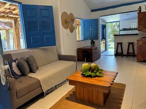 A living room with a sofa, a coffee table with fruit, and a kitchen area in the background. - Casa Moreira: Veranda & Beach 200m Away | Corumbau (Prado)