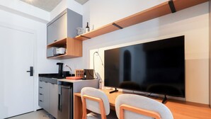 Eine kompakte Küche mit integriertem Geschirrspüler, einer Kaffeemaschine und einem flachbildfernseher an der Wand.