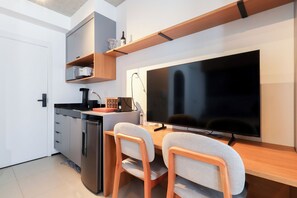 A compact kitchen with a built-in dishwasher, a coffee machine, and a flat-screen TV mounted on the wall. - Flat moderno perto do metrô e do Parque Ibirapuera (São Paulo)