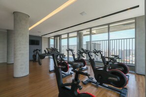 Ein Fitnessraum mit Cardiogeräten, großen Fenstern und Blick auf die Stadt.