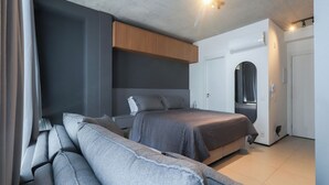 Ein modernes Schlafzimmer mit einem großen Bett, einer Couch, einem Kleiderschrank und einer Tür zu einem weiteren Raum.