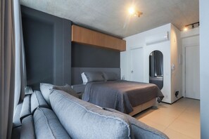 A modern bedroom with a large bed, a sofa, a wardrobe, and a door leading to another room. - Flat moderno perto do metrô e do Parque Ibirapuera (São Paulo)