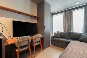 A modern hotel room with a large bed, a sofa, a TV, and a desk with two chairs. - Flat moderno perto do metrô e do Parque Ibirapuera (São Paulo)