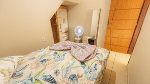 A bedroom with a bed, a bedside table, a fan, and a wardrobe. - Apto c/ Varanda,  Garagem e Vista das Montanhas (Angra dos Reis)