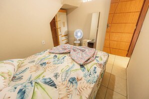 Ein Schlafzimmer mit Bett, Nachttisch, Ventilator und Kleiderschrank.