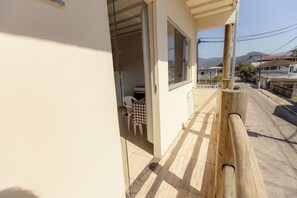 Ein schmaler Balkon mit Holzbalkon, einem karierten Tisch und einem Stuhl, mit Blick auf eine Straße mit Gebäuden und Bergen im Hintergrund.