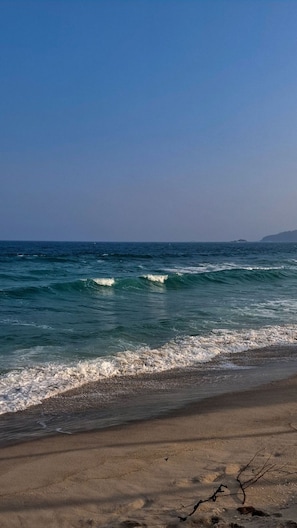Ein Strand mit ankommenden Wellen, einem klaren Himmel und entfernten Landformen.