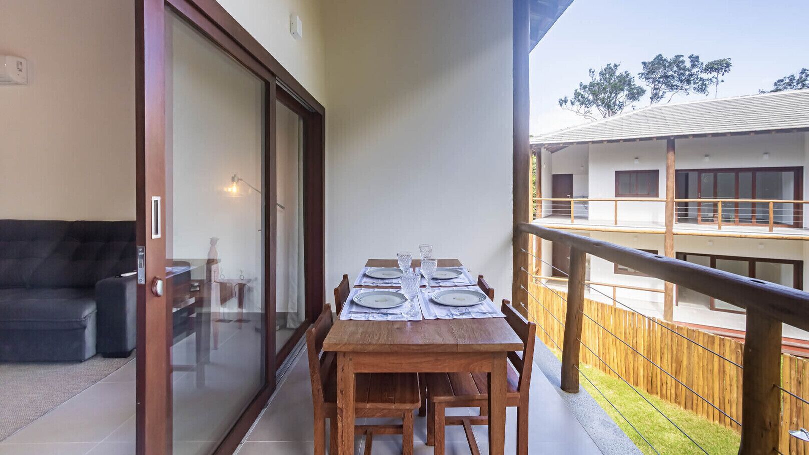 Varanda com uma mesa de jantar posta para quatro pessoas, uma porta de vidro deslizante e vista para um edifício do outro lado do jardim.
