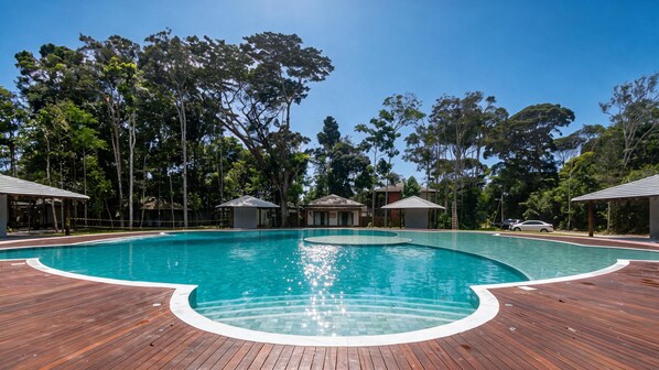 Una piscina con bordo in legno, circondata da alberi e piccoli edifici.