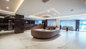 Een moderne hotellobby met een gebogen zithoek, een receptiebalie en een groot raam met uitzicht op buiten.