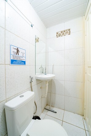 Une petite salle de bain propre, équipée de toilettes, d’un lavabo et d’un miroir. Un panneau est affiché sur le mur, avec des instructions rédigées en plusieurs langues.