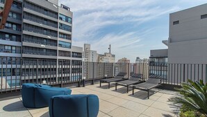 A rooftop terrace with seating, a view of surrounding buildings, and a clear sky. - Loft a 10min do metrô c Academia - Vila Mariana (São Paulo)
