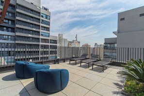 Eine Dachterrasse mit Sitzgelegenheiten und Blick auf die umliegenden Gebäude, strahlend blauer Himmel.