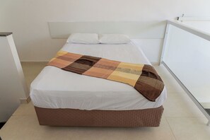 Ein Bett mit weißer Matratze und brauner Bettdecke, ein weißes Kopfteil und eine weiße Wand.